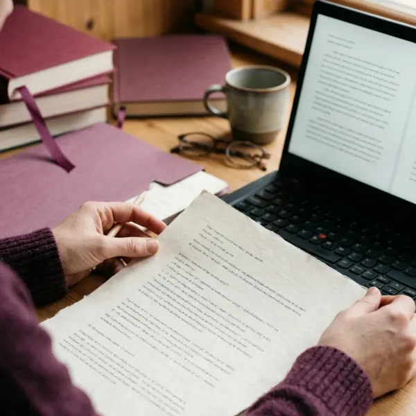 Hands holding a printed page next to a laptop screen to compare the two versions